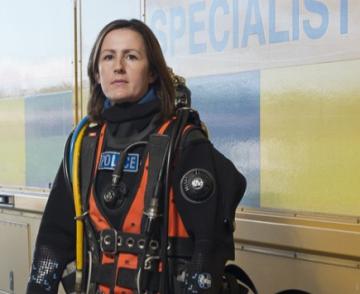 Lorna Dennison-Wilkins, in scuba gear in front of a police vehicle.